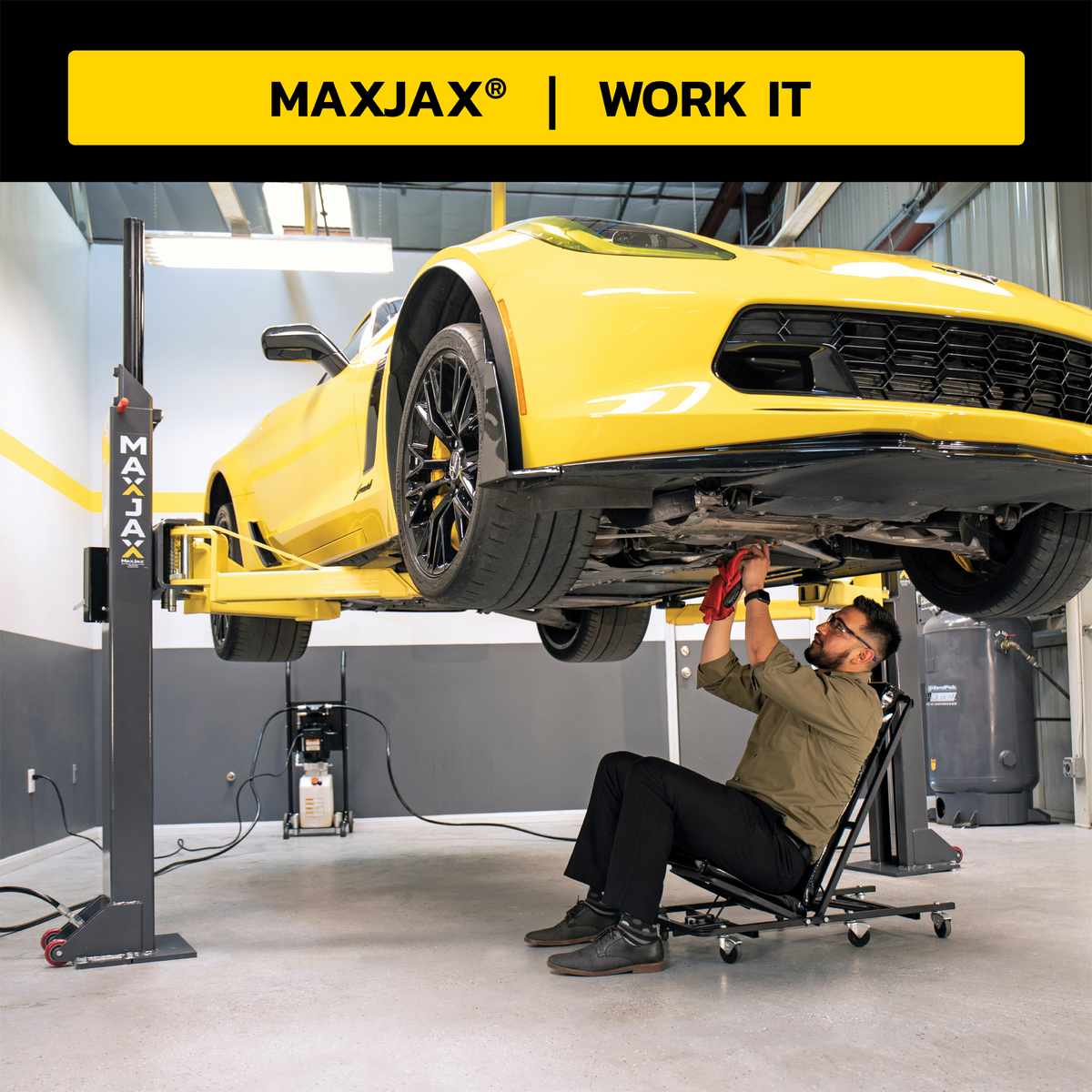 MaxJax portable car lift in use with a yellow sports car elevated; a technician working under the car while sitting on a rolling creeper seat, with a mobile power unit in the background.